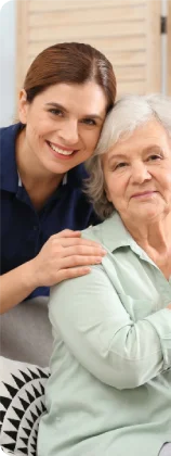 Caregiver smiling while resting her hand on an elderly woman's shoulder.