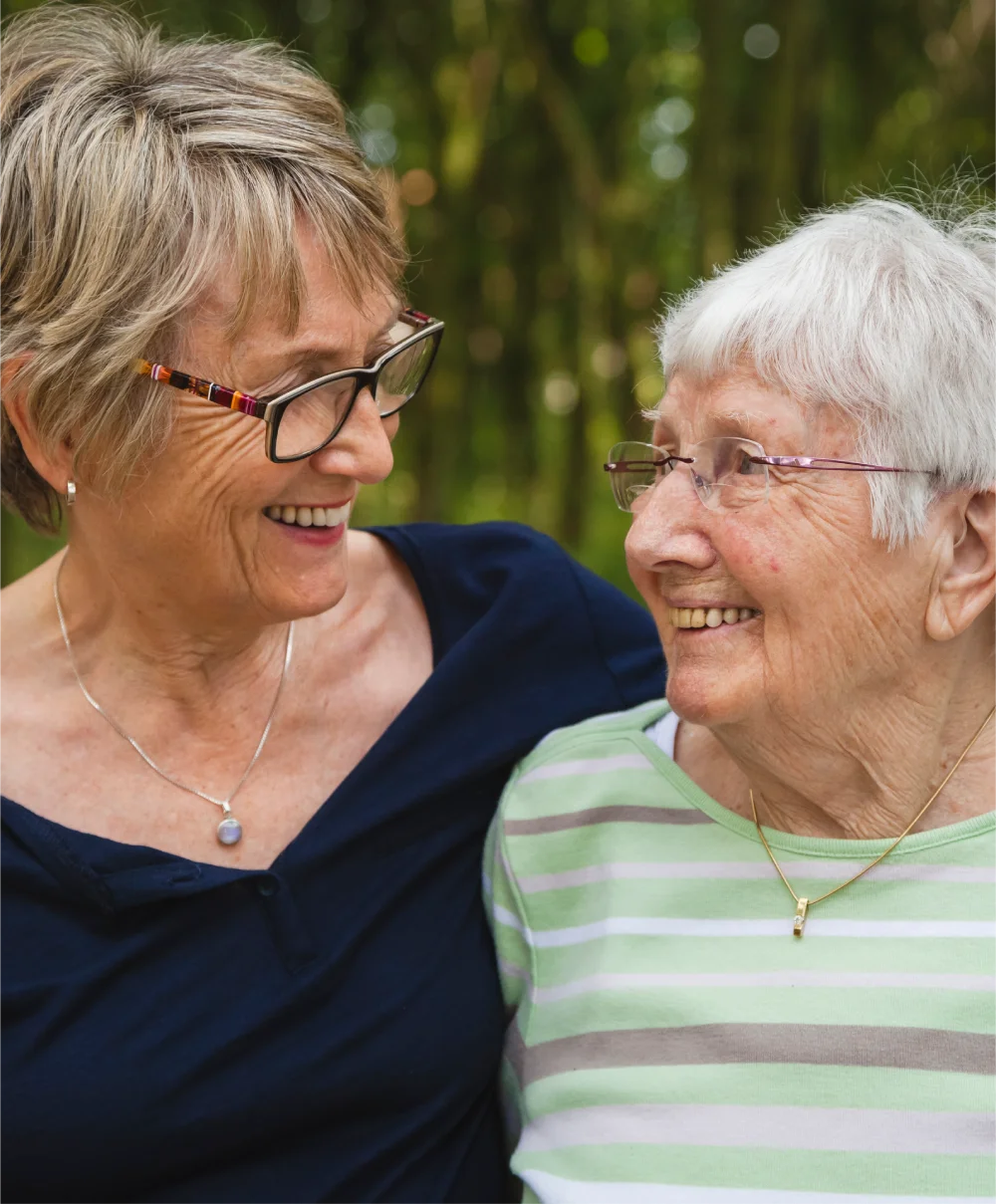 Two smiling women wearing glasses looking at each other outdoors.